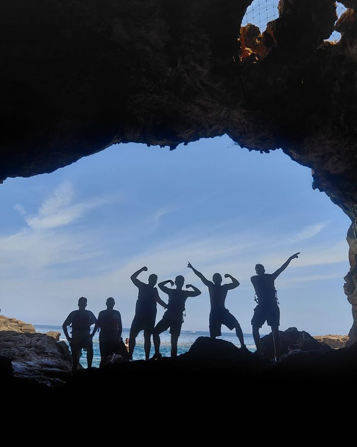 Siluetas de un grupo de amigos saltando en la boca de una cueva frente al mar